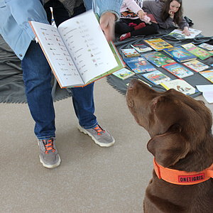 Welttag des Buches. Grundschüler veranstalten Bücherflohmarkt in der neuen Aula. Schulhund Carlos liest ein Buch..